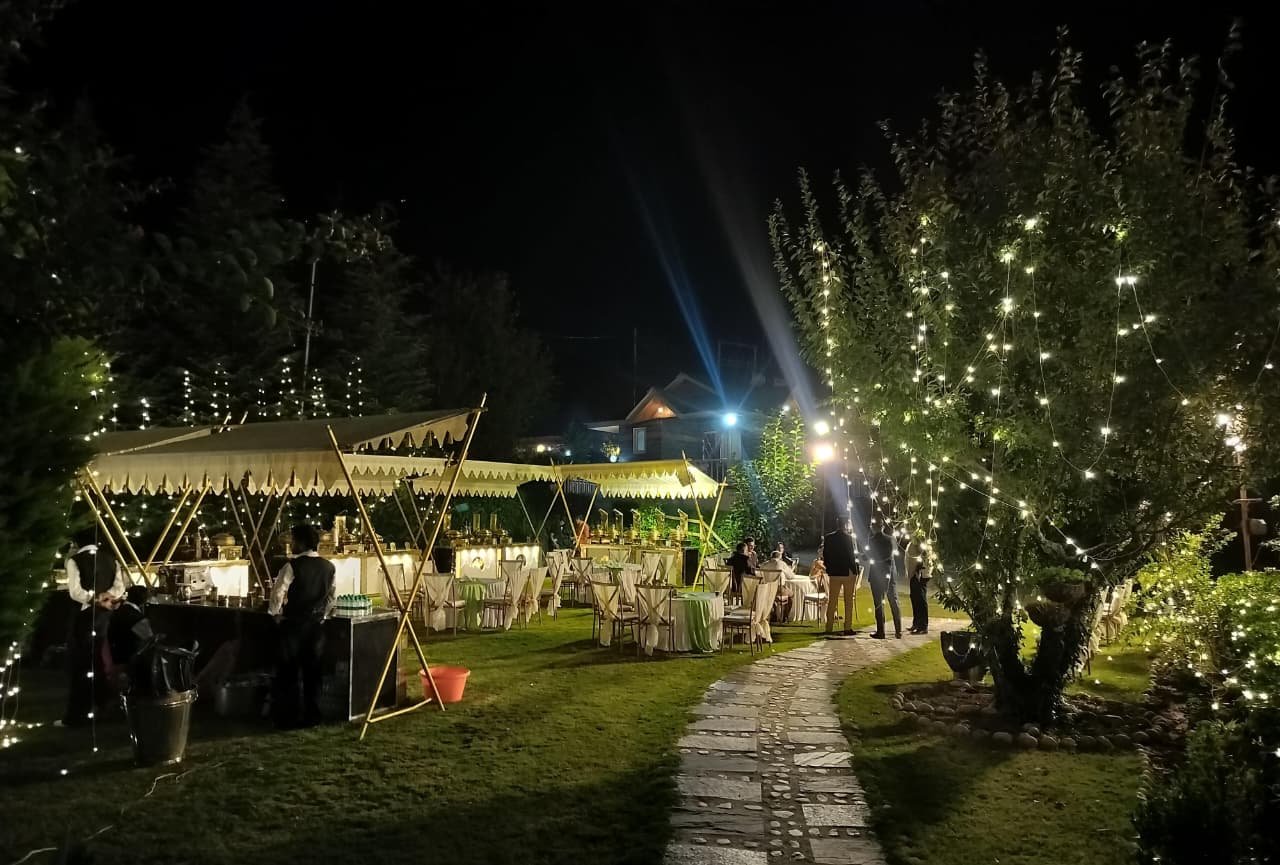 Buffet counters, lit apple tree and stone garden path at night at Shree Ganga Cottages