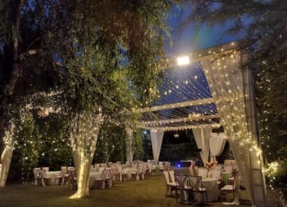 Ring ceremony setup at dusk with fairy lights, draped pillars and round tables on the lawn of Shree Ganga Cottages, Raison Kullu